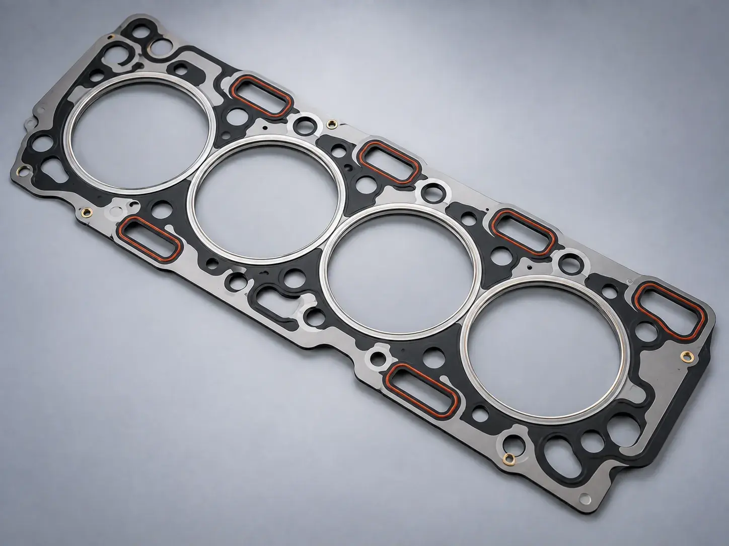 A new multi-layer steel cylinder head gasket laid flat, its four bores visible